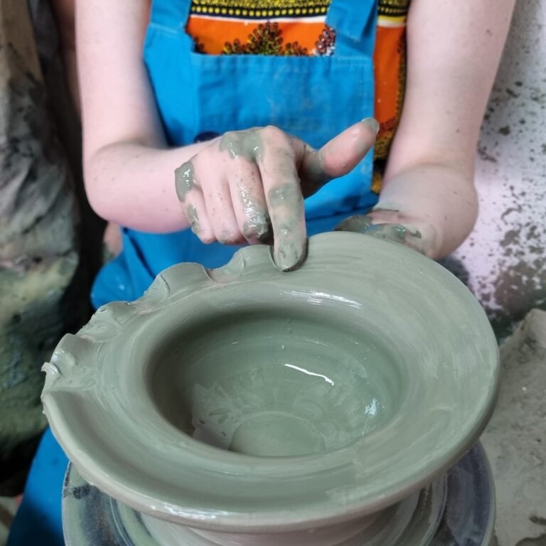 hands decorate a clay pot during pottery class
