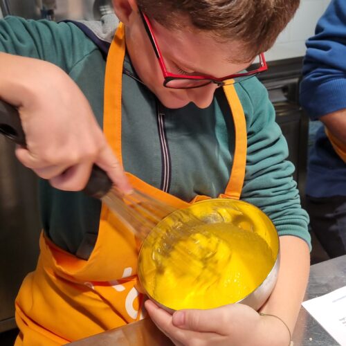 Child preparing cream by hand during short pastry cooking class