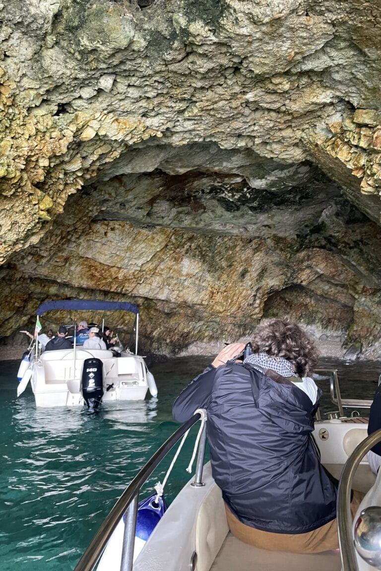 Guests photographing the sea caves of Polignano a Mare during a boat excursion, surrounded by colourful rock formations and crystal-clear water