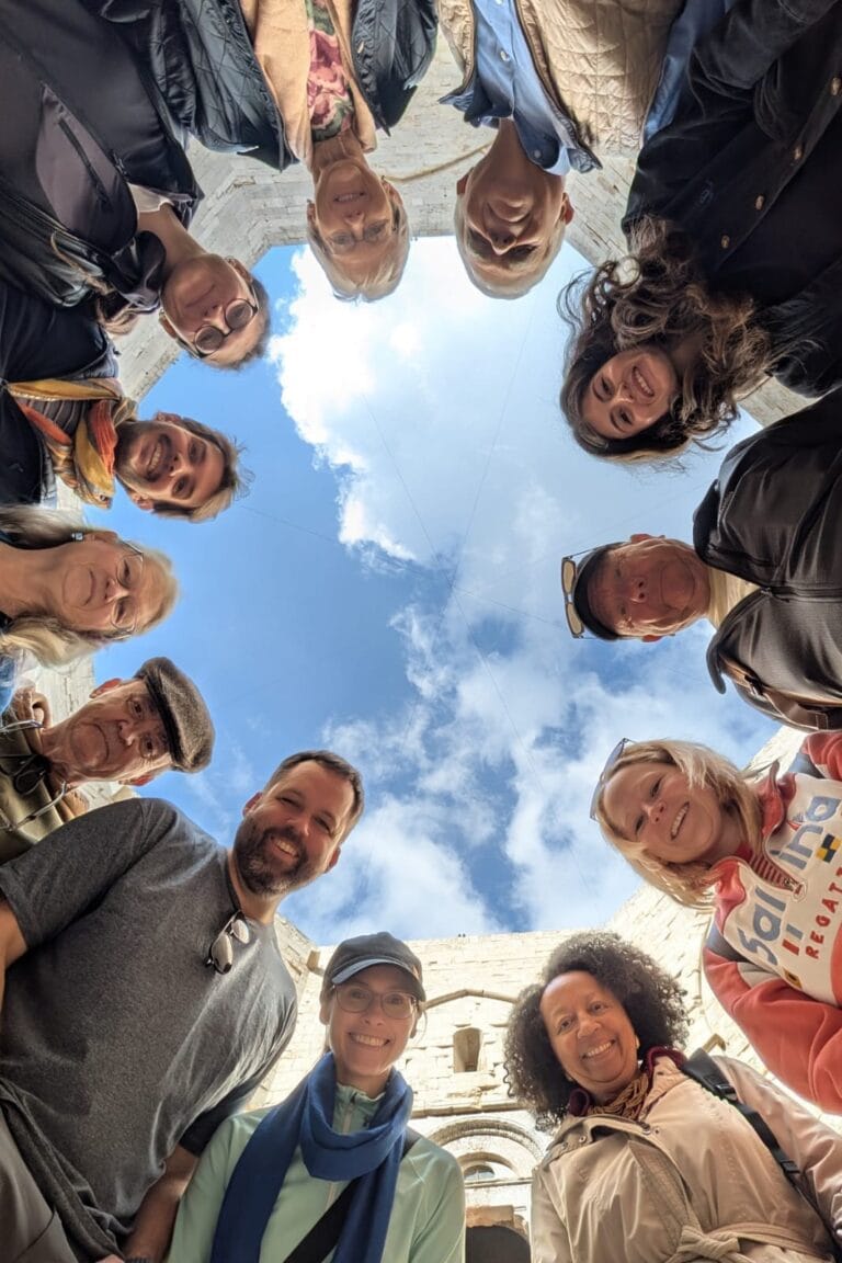 Group of travellers gathered in a circle under the bright Apulian sky, surrounded by the ancient stones of Castel del Monte