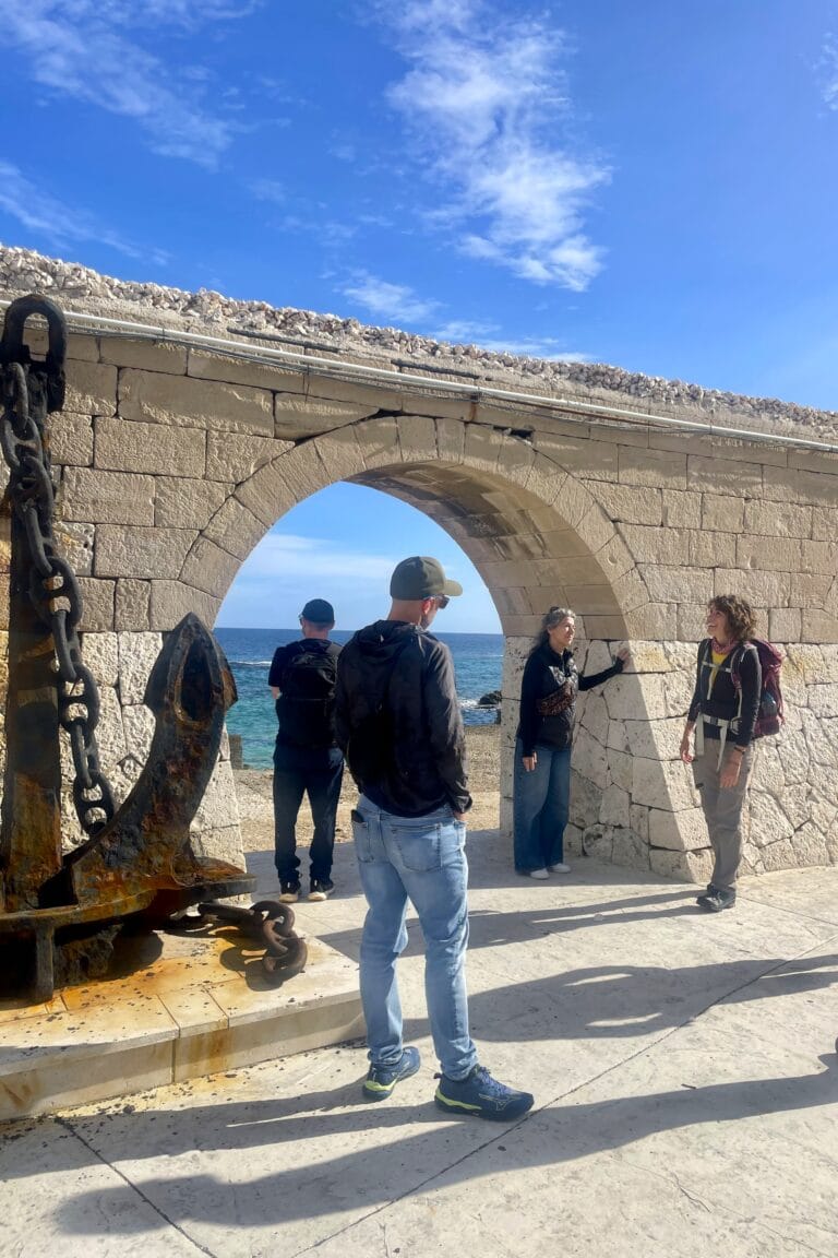 Travellers observing the Apulian coastline through a stone arch overlooking the sea, while learning about the history of the site