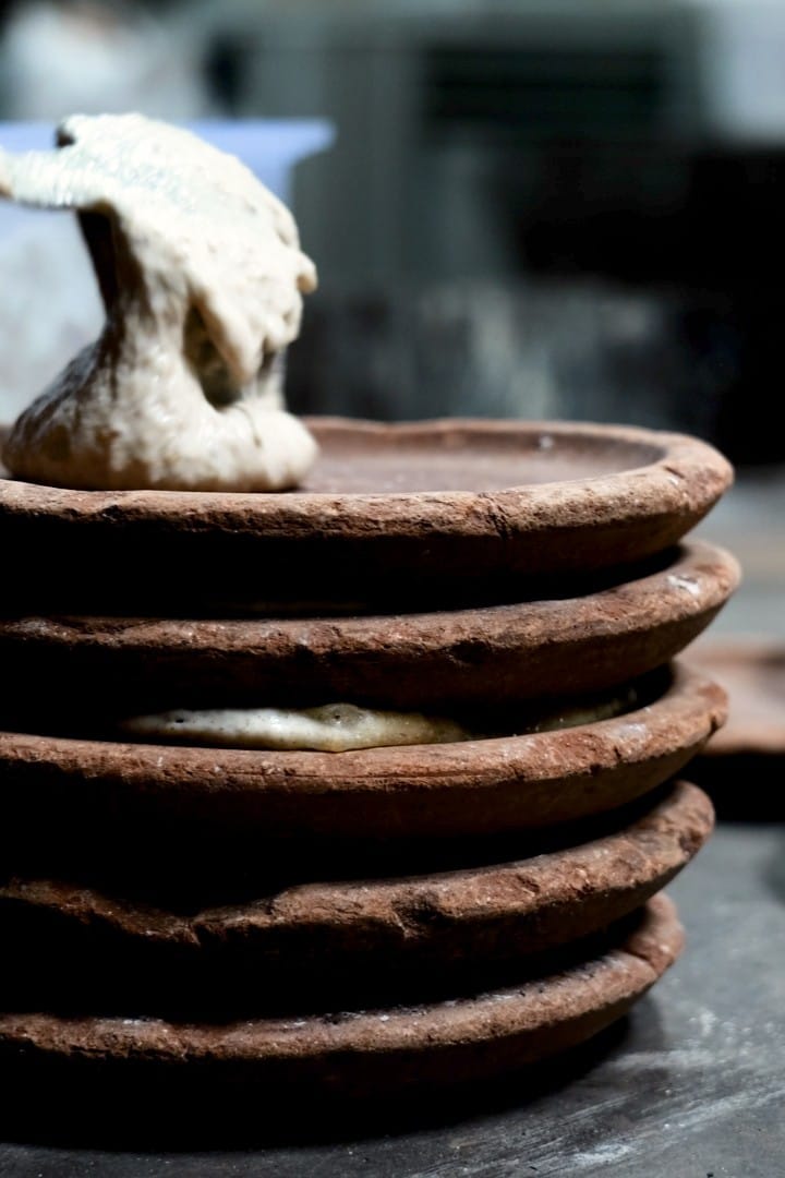 Panigacci baking between clay plates in a traditional wood-fired oven